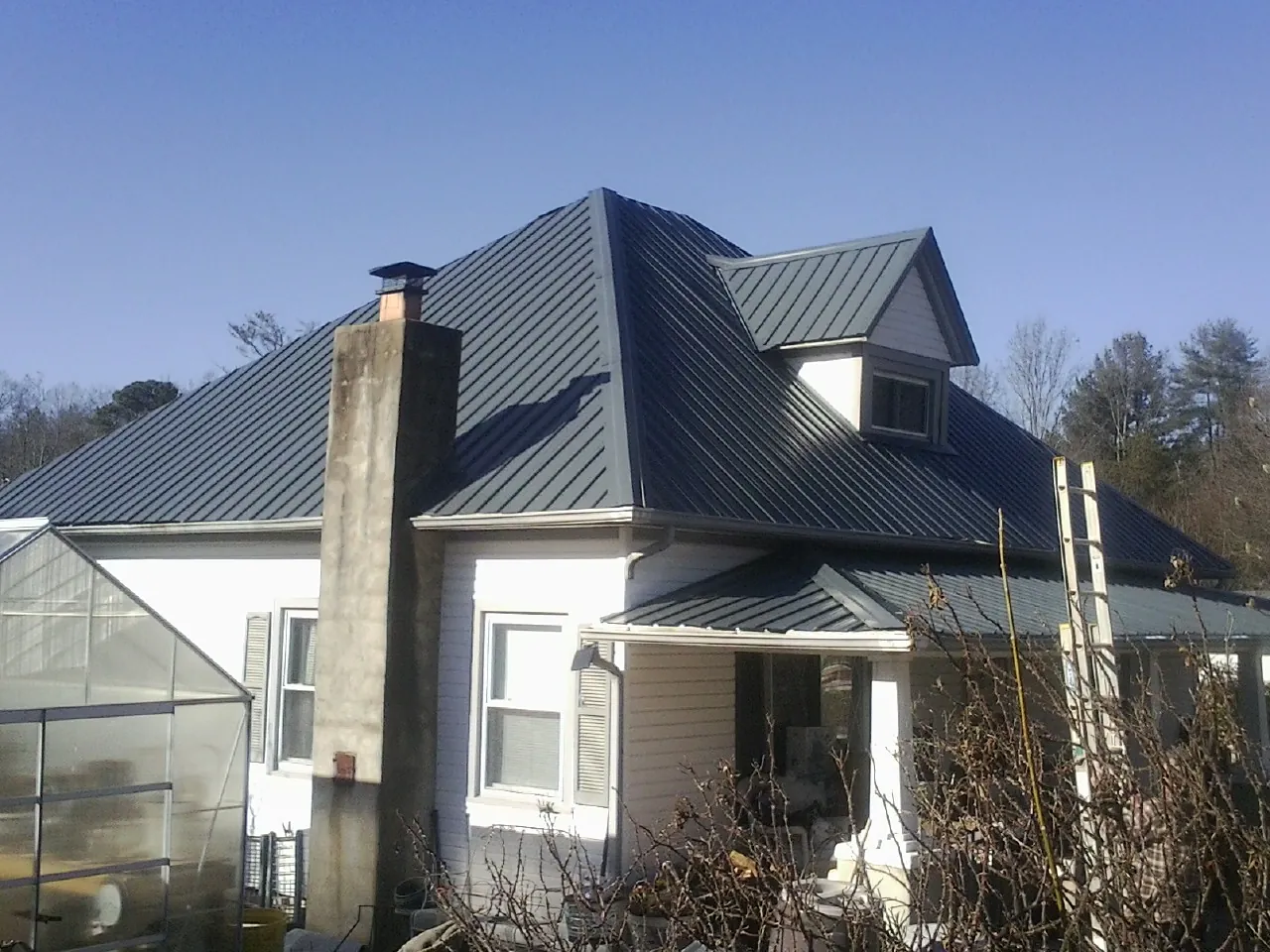 Dark blue standing seam metal roof on a white farmhouse with dormer in Elon