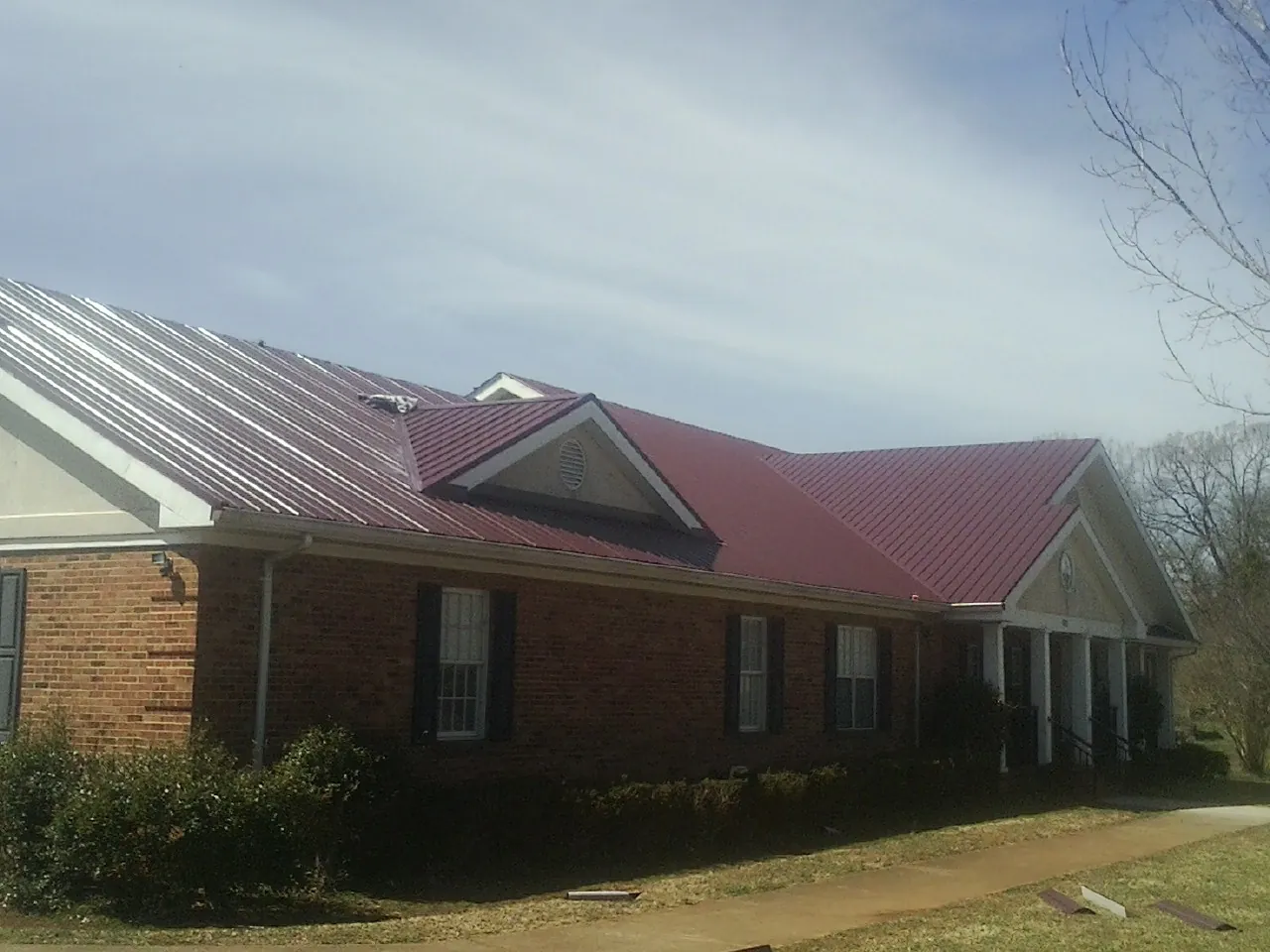 Red metal roof with gabled entries on a long brick building, from a Hail Damage Roof Repair job in Elon