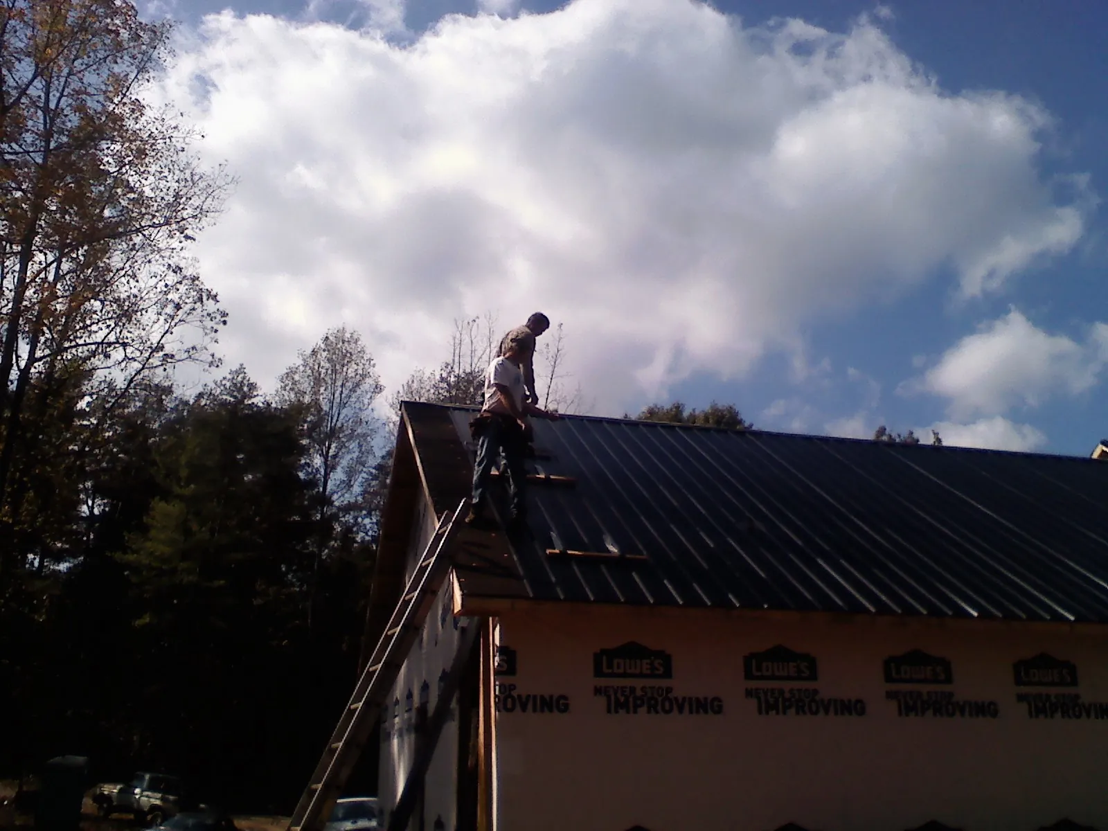 Roofer fastening dark metal panels high against a cloudy sky, from a Roof Inspection job in Elon