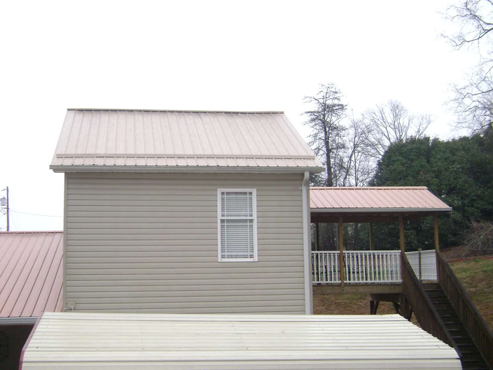 Tan metal roofs on a two story addition and attached porch, from a Roof Replacement job in Elon